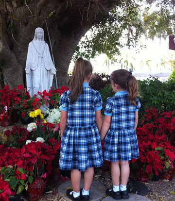 Two School girls stand in front of a Mary Statue praying